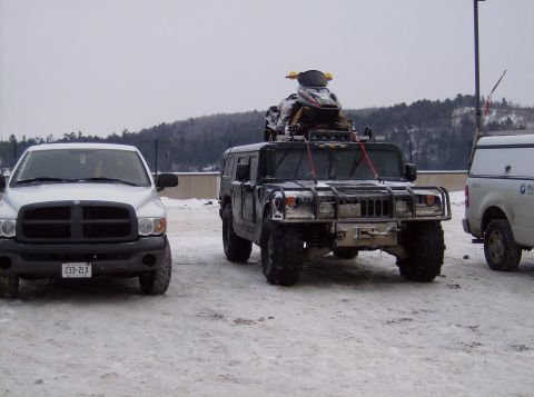 1981 Ford Bronco - A Humvee carrying a snowmobile is parked in a snowy area next to other vehicles.