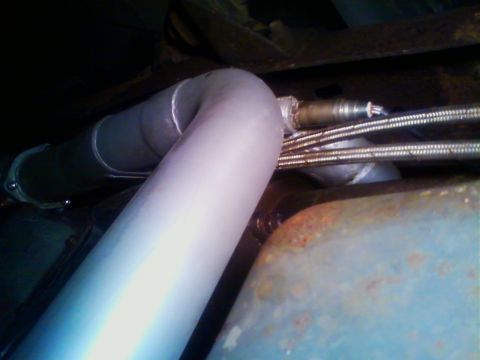 1990 Ford Bronco - Underbody close-up of a newly installed aluminized Y-pipe with two inlet legs merging, shot from below alongside a rusty floor pan and fram…