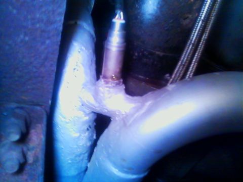 1990 Ford Bronco - Tight underbody shot of an exhaust Y-pipe junction, with two aluminized tubes merging into a welded collector and an oxygen sensor threaded…