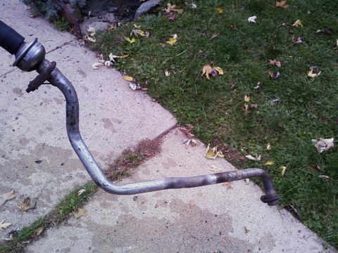 1990 Ford Bronco - An exhaust pipe component, likely from a vehicle, lies on a concrete and grass surface.