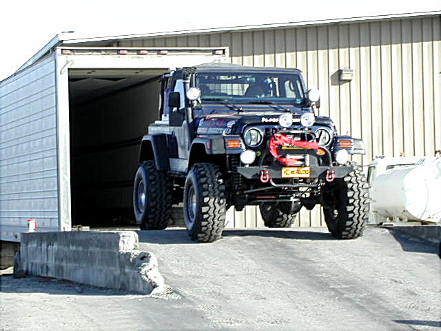 Dark blue lifted Jeep with big tires and winch at a metal building doorway