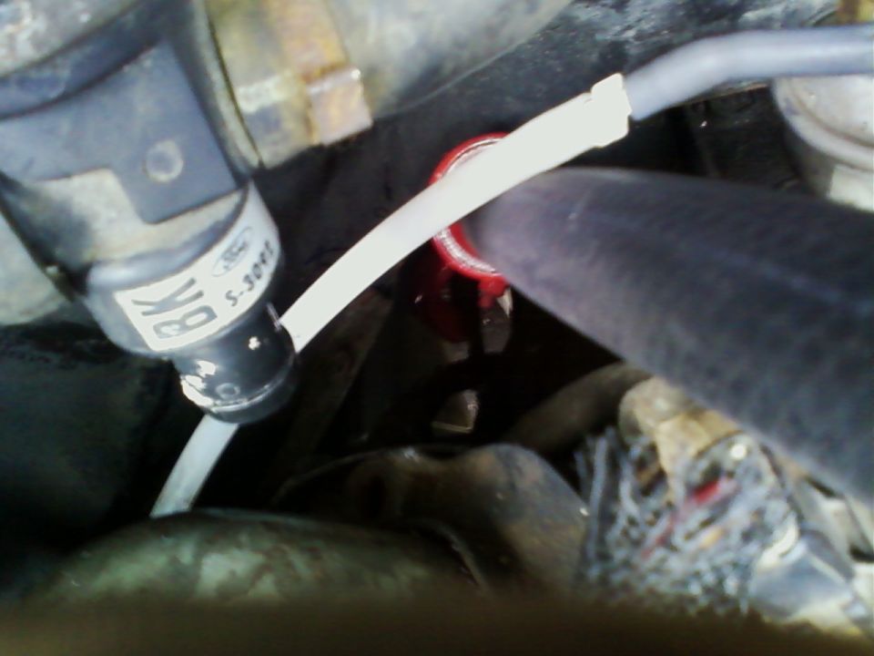Close-up of a black Ford vacuum solenoid with a white vacuum hose in an engine bay