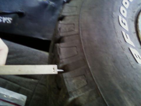 1990 Ford Bronco - A caliper measures the tread depth of a tire, with a "Supermotors" logo in the corner.