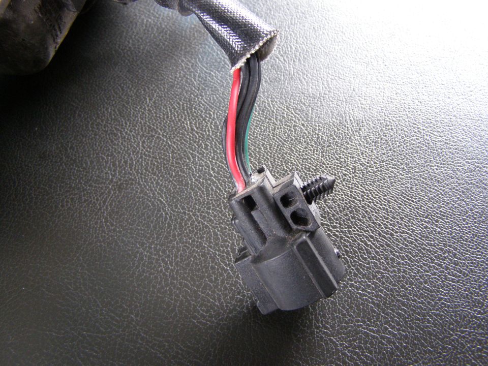 Electrical connector with red, black, and green wires attached to a black plastic housing with a screw. Textured dark surface