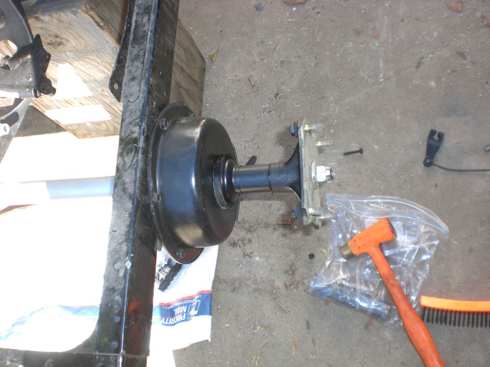 Black drum hub and shaft assembly with mounting bracket on concrete floor beside orange hammer and Priority Mail envelope