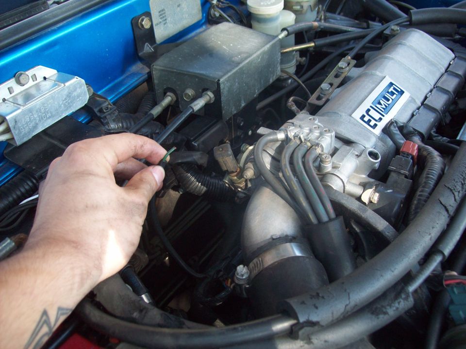 Close-up of engine bay with hand reaching for a wire harness; ECM MULTI label visible