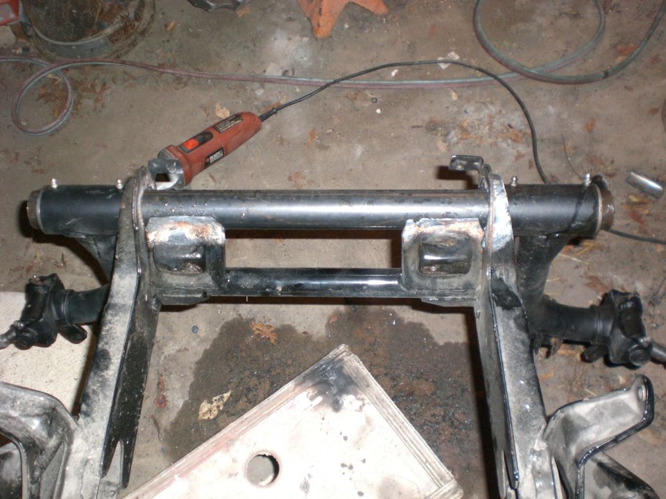 Black swingarm and axle assembly on garage floor with a red rotary tool resting on it