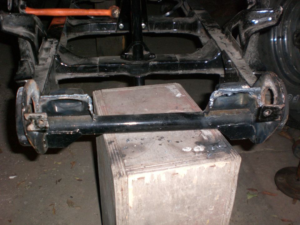 Underside view of a vehicle frame and rear axle with a wooden box beneath