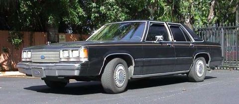 1991 Ford Crown Victoria - This black Ford sedan, likely from the 1980s, is viewed from a three-quarter front angle.