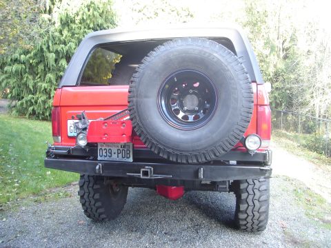1989 Ford Bronco - The rear of a red SUV is shown, a spare tire, a custom bumper, and a license plate.