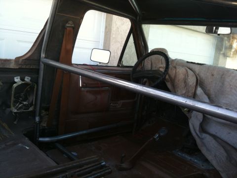 1982 Ford Bronco - The interior of a vehicle is shown with a prominent roll cage and a cloth covering the passenger seat.
