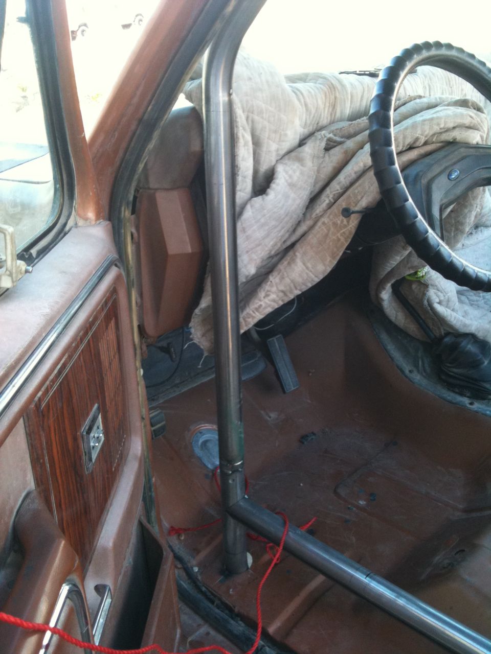 Interior view of a vehicle showing a metal roll cage installed, with a blanket covering the passenger seat and dashboard