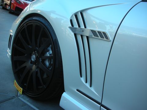 1998 Ford Crown Victoria - Close-up of a white car's fender and wheel, with another car in the background.