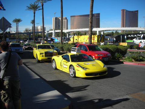 1998 Ford Crown Victoria - bright yellow Ferrari leads a yellow Rolls-Royce down a palm-lined street with Las Vegas hotel towers in the background.