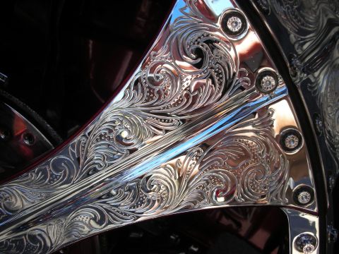 1998 Ford Crown Victoria - Extreme close-up of intricate floral scrollwork engraving on a polished chrome wheel with small gem-set rivets.