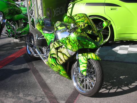 1998 Ford Crown Victoria - custom sportbike with green-and-black airbrushed graphics and chrome forks displayed near an Xbox booth backdrop.