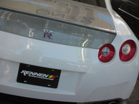 1998 Ford Crown Victoria - Close rear three-quarter of a white Nissan GT-R showing its GT-R badge, carbon spoiler and round taillights above a Rennen plate.