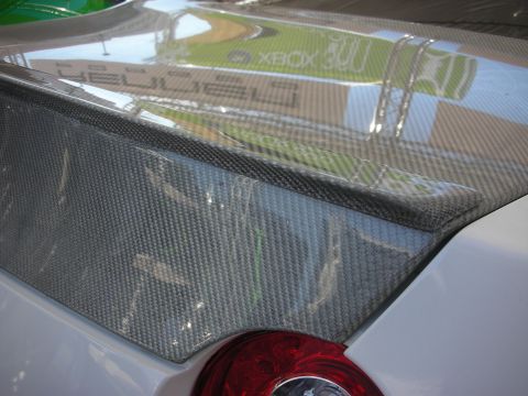 1998 Ford Crown Victoria - Detail of a carbon-fiber rear spoiler mounted on a silver car, with red taillight and event reflections visible.