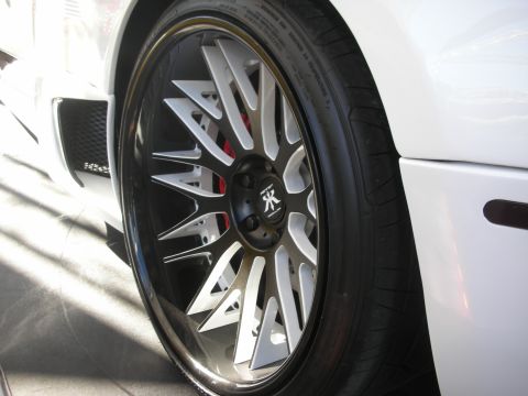 1998 Ford Crown Victoria - black-and-machined multi-spoke wheel with a red brake caliper mounted on a white car, low-profile tire fitted.