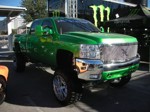 1998 Ford Crown Victoria - green lifted Chevrolet Silverado HD crew-cab pickup on a tall suspension and chrome wheels under a Monster Energy tent.