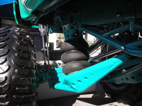 1998 Ford Crown Victoria - Undercarriage of a lifted truck showing stacked airbag springs, teal control arms and a deep off-road tire tread.