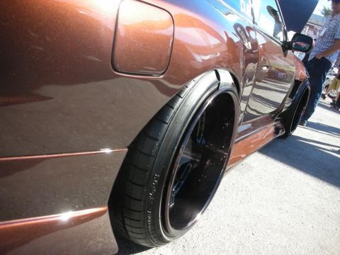 1998 Ford Crown Victoria - Close-up of a brown metallic custom car's rear fender flare and a deep-dish black wheel with stretched tire.