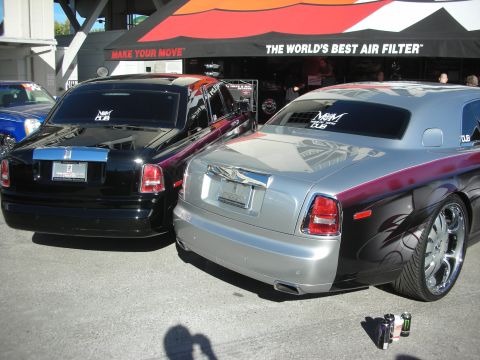 1998 Ford Crown Victoria - Two custom Rolls-Royce sedans, one black and one two-tone silver-and-maroon, parked under an air-filter branded canopy.