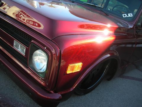 1998 Ford Crown Victoria - Close-up of the maroon front fender, single round headlight and grille of a slammed classic pickup truck.