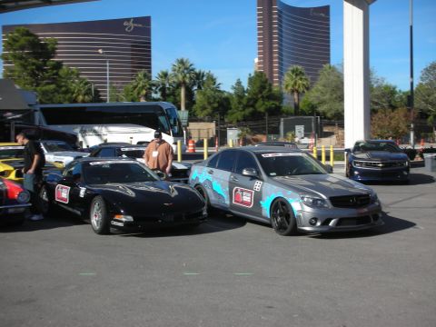 1998 Ford Crown Victoria - black Corvette and a wrapped silver Mercedes sedan parked at an event with high-rise hotels behind.