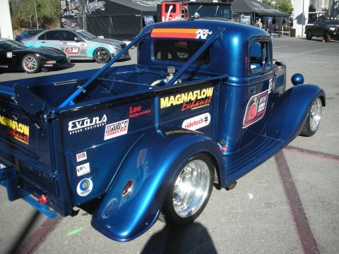 1998 Ford Crown Victoria - Rear three-quarter view of a blue vintage hot-rod pickup covered in sponsor decals with polished alloy wheels.