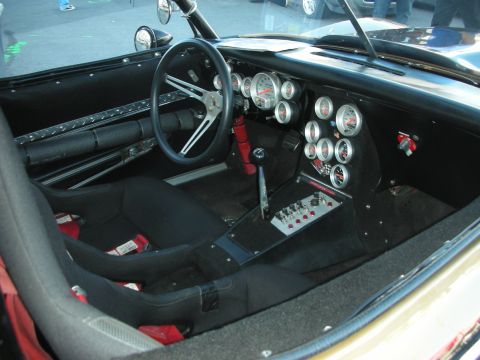 1998 Ford Crown Victoria - Bare race-car interior with a three-spoke steering wheel, bank of round gauges, switches and a bucket seat.