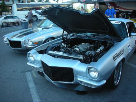 1998 Ford Crown Victoria - Two early-1970s Camaros at an outdoor show; the silver foreground car has its hood up exposing the engine.