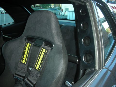 1998 Ford Crown Victoria - black bucket seat fitted with a yellow Schroth racing harness next to a padded roll-cage door bar.
