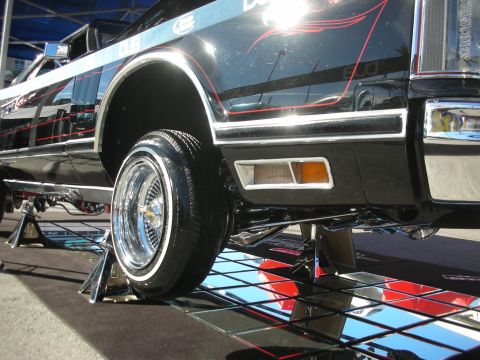 1998 Ford Crown Victoria - Low-angle shot of a black custom car's chrome wire wheel and whitewall tire raised on a display stand over a mirrored floor.
