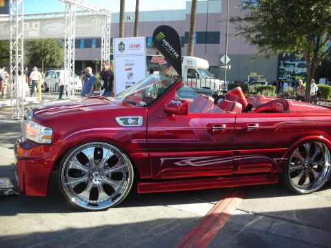 1998 Ford Crown Victoria - candy-red convertible with red leather interior and large chrome wheels sits on display at an outdoor car show.