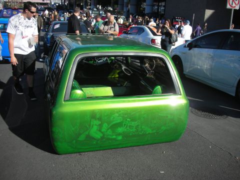 1998 Ford Crown Victoria - Rear three-quarter of a lowered green SUV with airbrushed figural murals, parked among people at an outdoor car show.