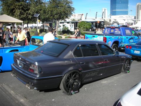 1998 Ford Crown Victoria - slammed dark gray BMW 7 Series sedan on black wheels with wheel stands sits parked at an outdoor automotive event.