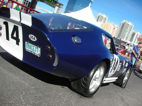 1998 Ford Crown Victoria - blue-and-white race coupe wearing number 14 and a vanity plate reading I RACE IT sits outdoors with a city skyline behind.