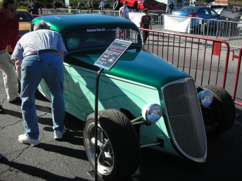 1998 Ford Crown Victoria - green flamed Factory Five-style hot rod coupe with exposed front wheels at a car show as a man leans into the cockpit.