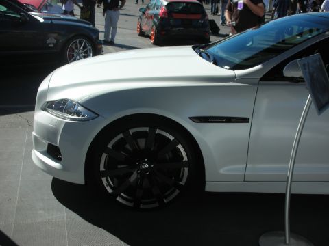 1998 Ford Crown Victoria - Front fender and door of a white Jaguar XJ sedan on two-tone turbine-style wheels at an outdoor display.