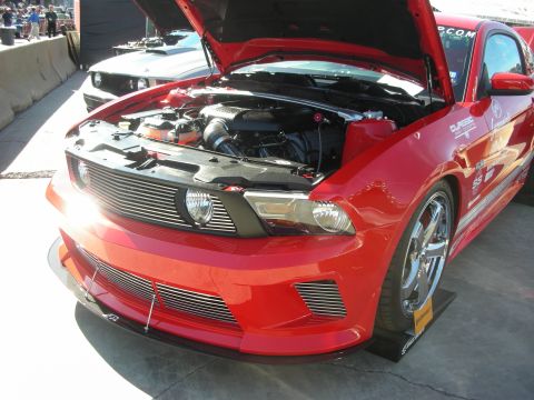 1998 Ford Crown Victoria - red Mustang coupe with open hood shows front-mount intercooler piping and chrome wheels on display at an outdoor show.