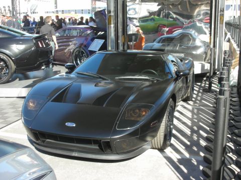 1998 Ford Crown Victoria - matte black mid-engine supercar bearing a Ford emblem, displayed indoors among other cars at a show.