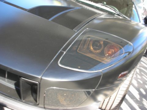 1998 Ford Crown Victoria - Close-up detail of a matte black supercar's front fender, projector headlight and racing stripe.