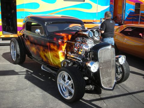 1998 Ford Crown Victoria - black three-window hot rod with fire-flame paint, exposed chrome V8 and chrome grille at an outdoor show.
