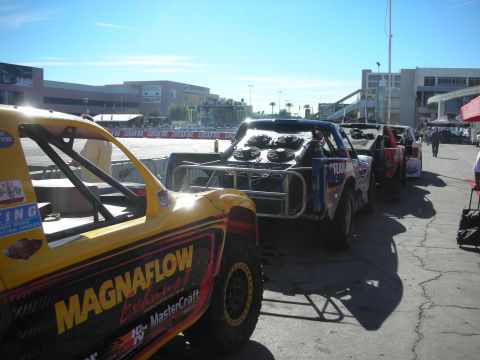1998 Ford Crown Victoria - row of off-road race trucks with Magnaflow and other sponsor decals staged outdoors under blue sky.