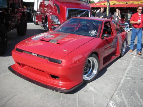1998 Ford Crown Victoria - red widebody sports coupe with pop-up headlights and a Toyota nose badge at an outdoor show.