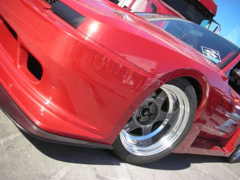 1998 Ford Crown Victoria - Low-angle close-up of a red widebody car's front fender, polished-lip wheel and carbon front splitter.