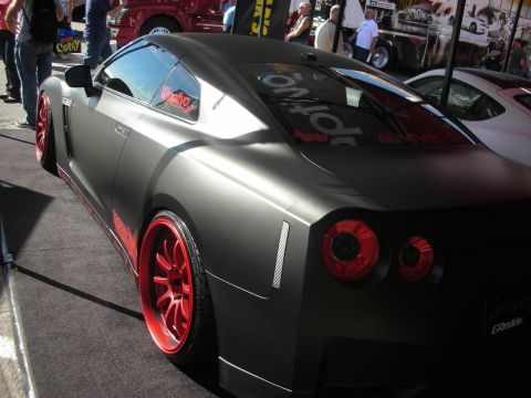 1998 Ford Crown Victoria - Rear three-quarter of a matte gray Nissan GT-R with red wheels and quad round taillights at a show.