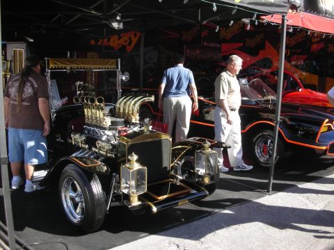 1998 Ford Crown Victoria - black-and-gold T-bucket hot rod with tall velocity stacks and carriage lamps displayed beside a Batmobile.