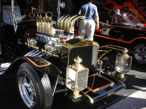 1998 Ford Crown Victoria - gold-and-black T-bucket hot rod with tall brass velocity stacks and ornate carriage lamps at a show.